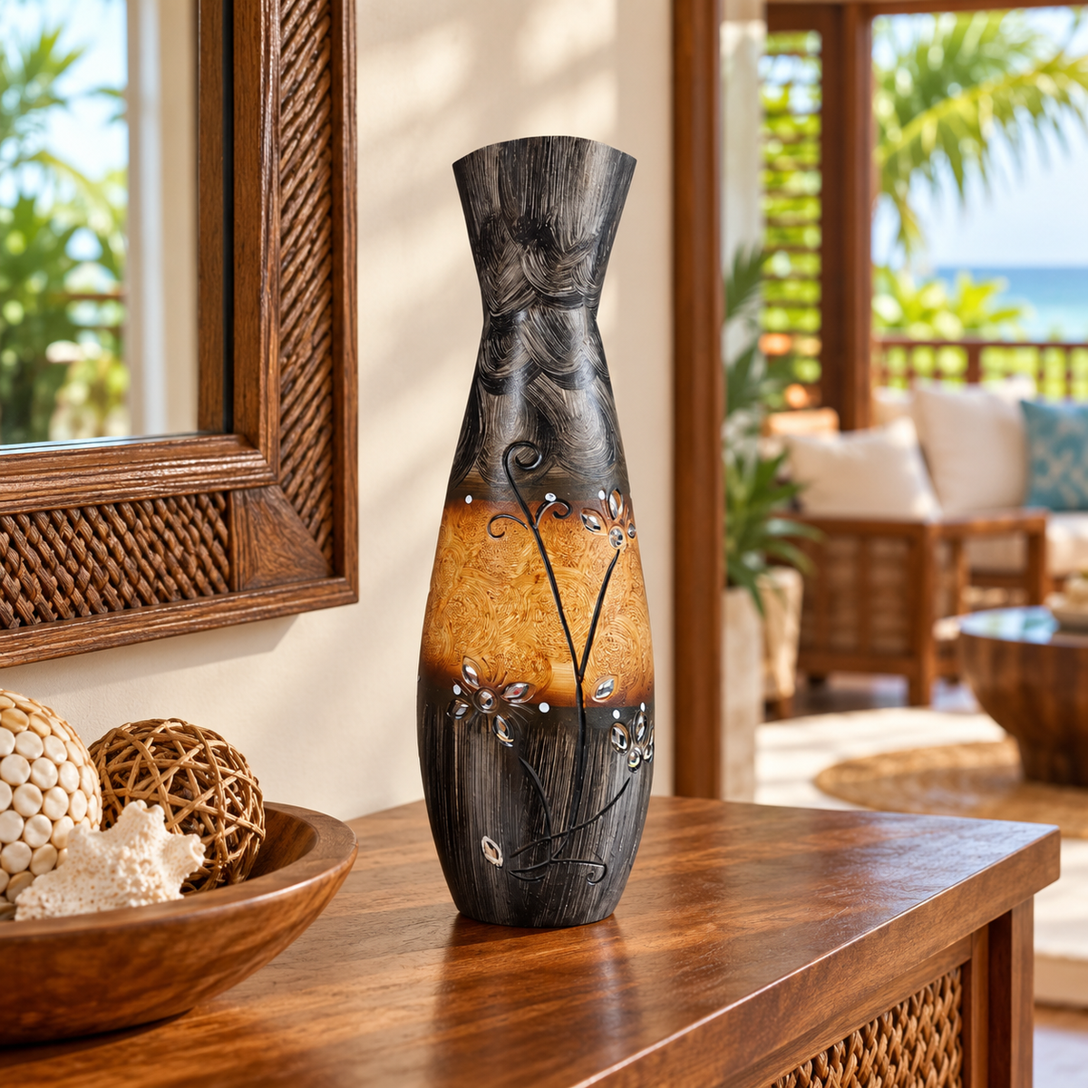 A decorative ceramic vase with a dark textured top half and a warm amber-brown glazed bottom half, decorated with white floral details and small metallic silver accents, displayed on a wooden console table in a tropical patio setting.